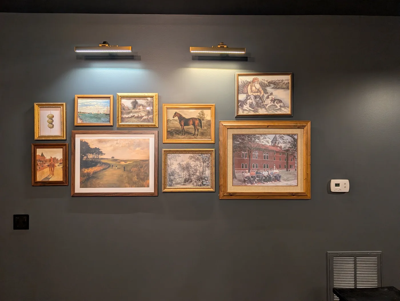 Framed artwork arranged and mounted on a dark wall by Frye Inc.