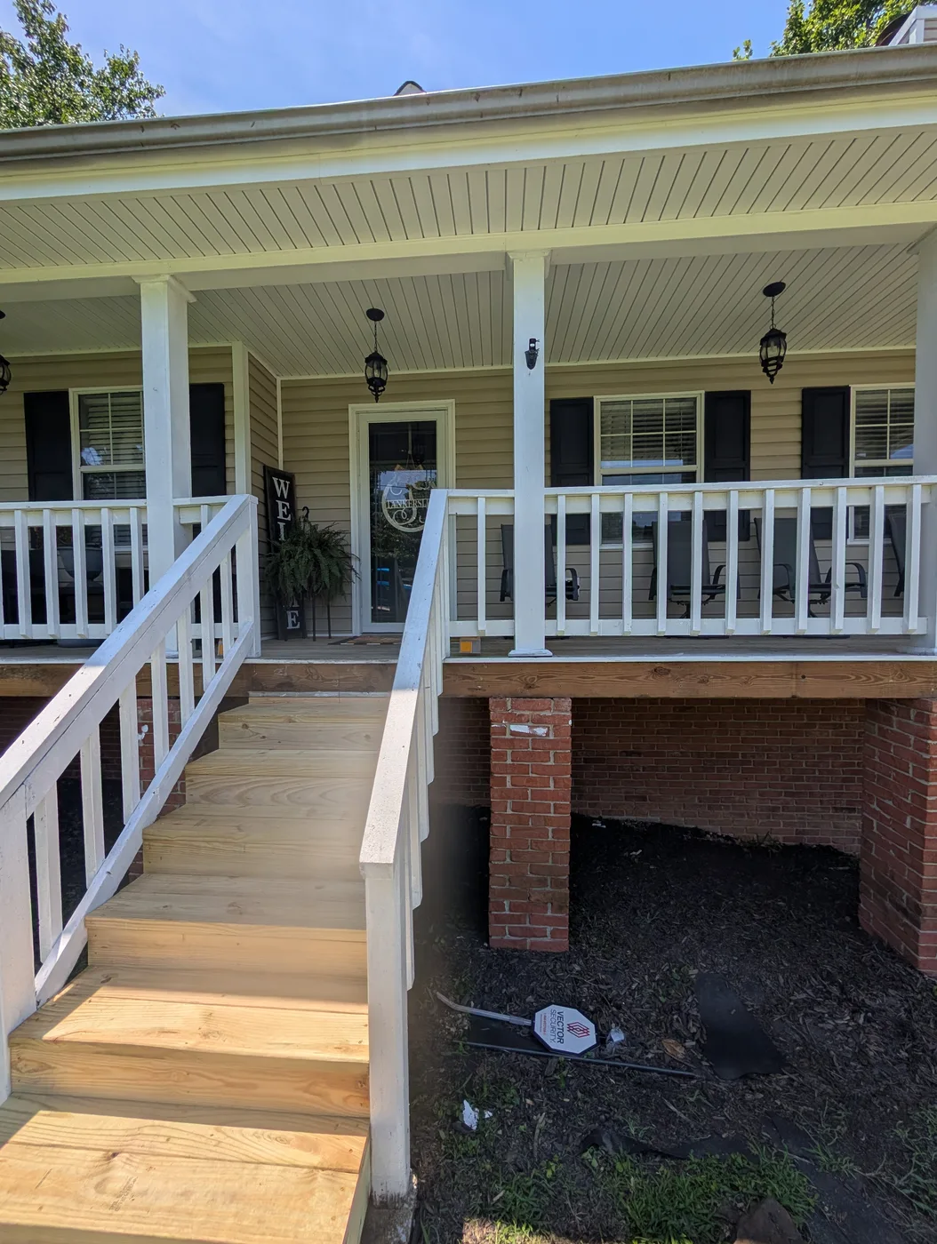 Wood front porch steps with white railings beside a brick foundation, from a Frye Inc. project